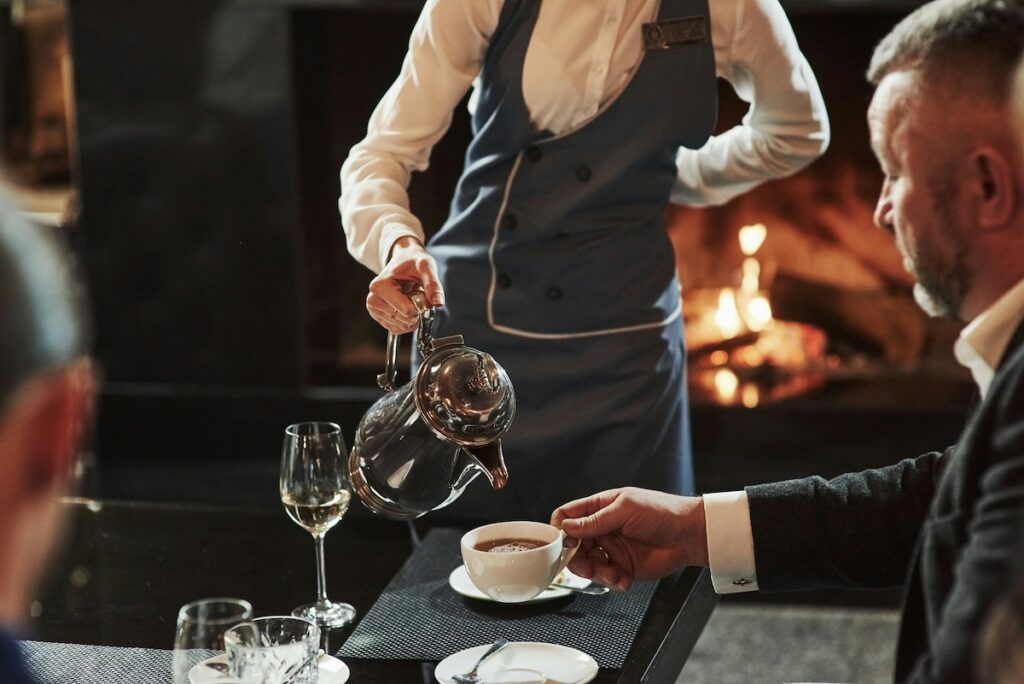 A waiter pours coffee next to a glass of wine