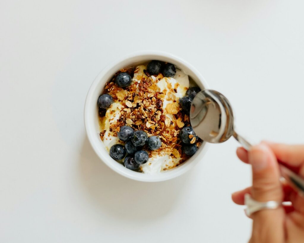 Woman decides to eat a sweet treat of blueberries, yogurt, and granola after intermittent fasting