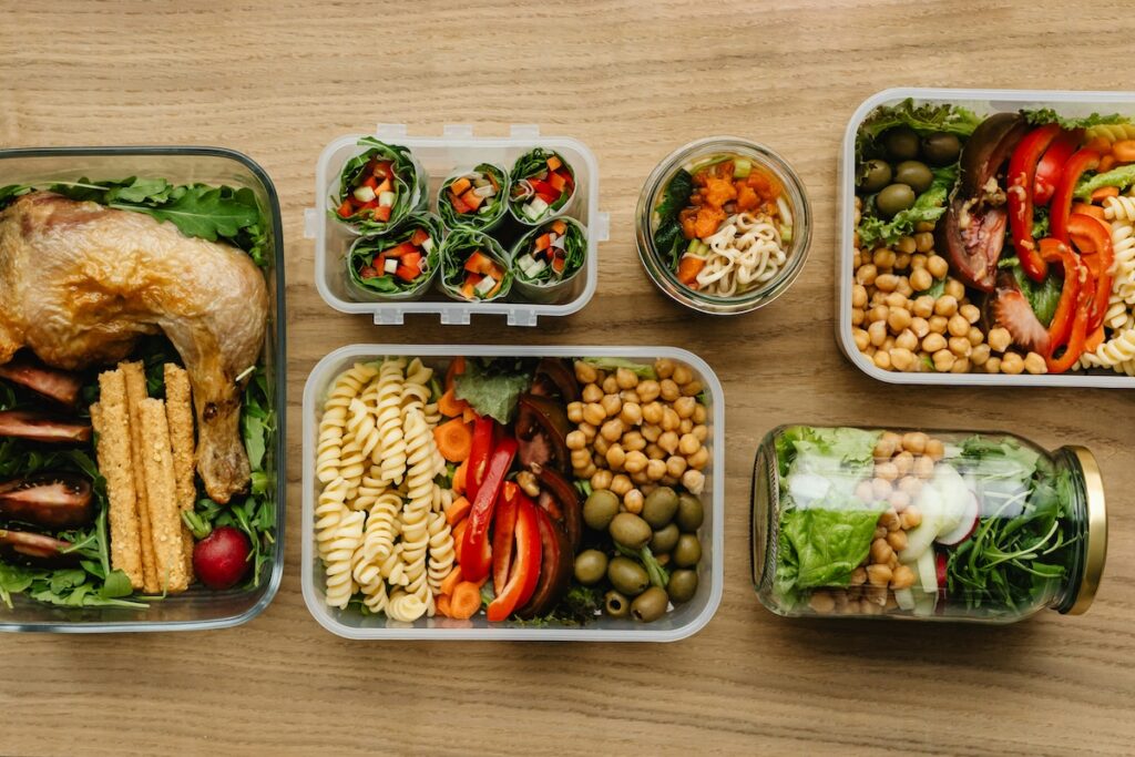 Meal-prep containers with high protein lunch ideas including chicken, pasta salad, veggie wraps, and chickpea jars