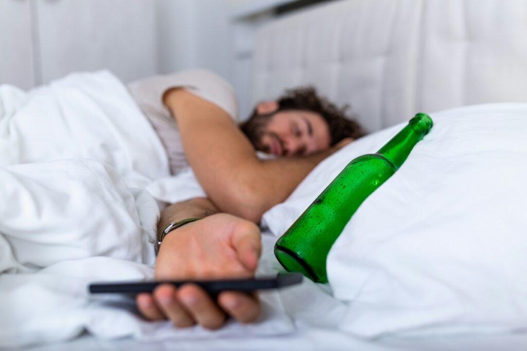 Man sleeping in bed after a night of drinking, with an empty beer bottle nearby, illustrating how to restore gut health after alcohol