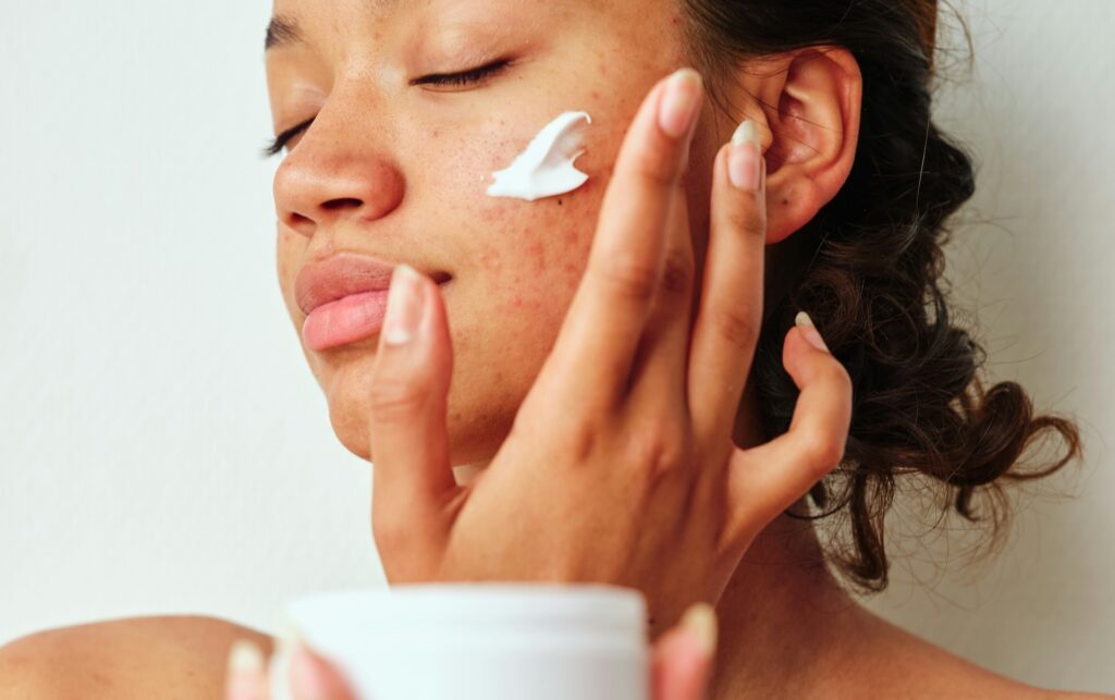 a woman with acne-prone skin applying Benzoyl Peroxide Benzene to her cheek from a jar