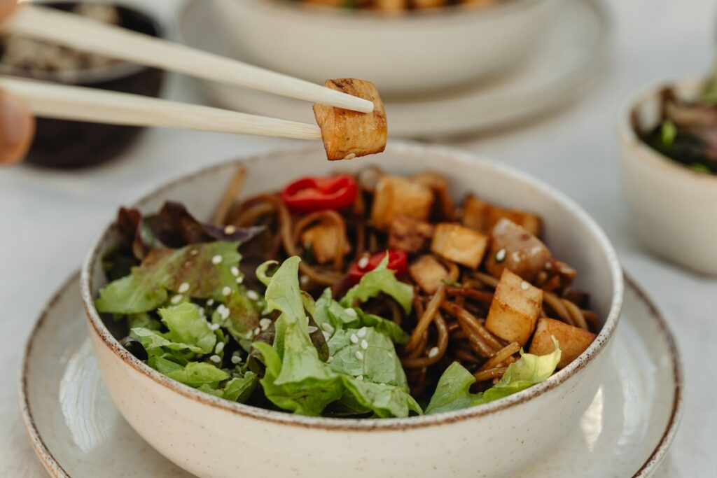 Person picks up crispy, flavorful cube of tofu from a low-calorie bowl of tofu and greens. 