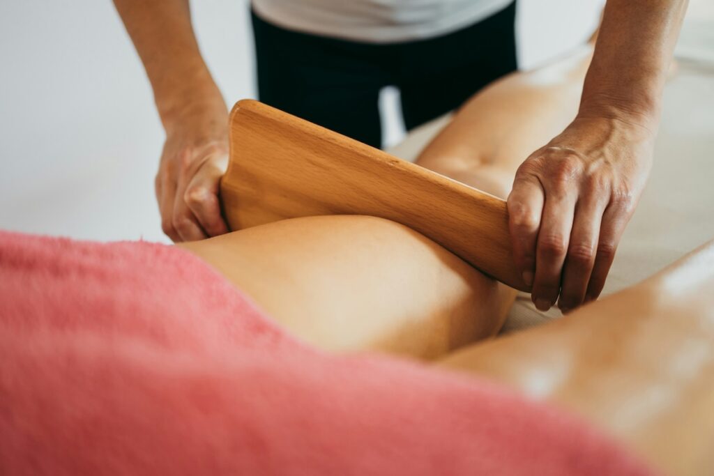 a therapist using a wooden lymphatic drainage tool to massage a client's leg during a body treatment
