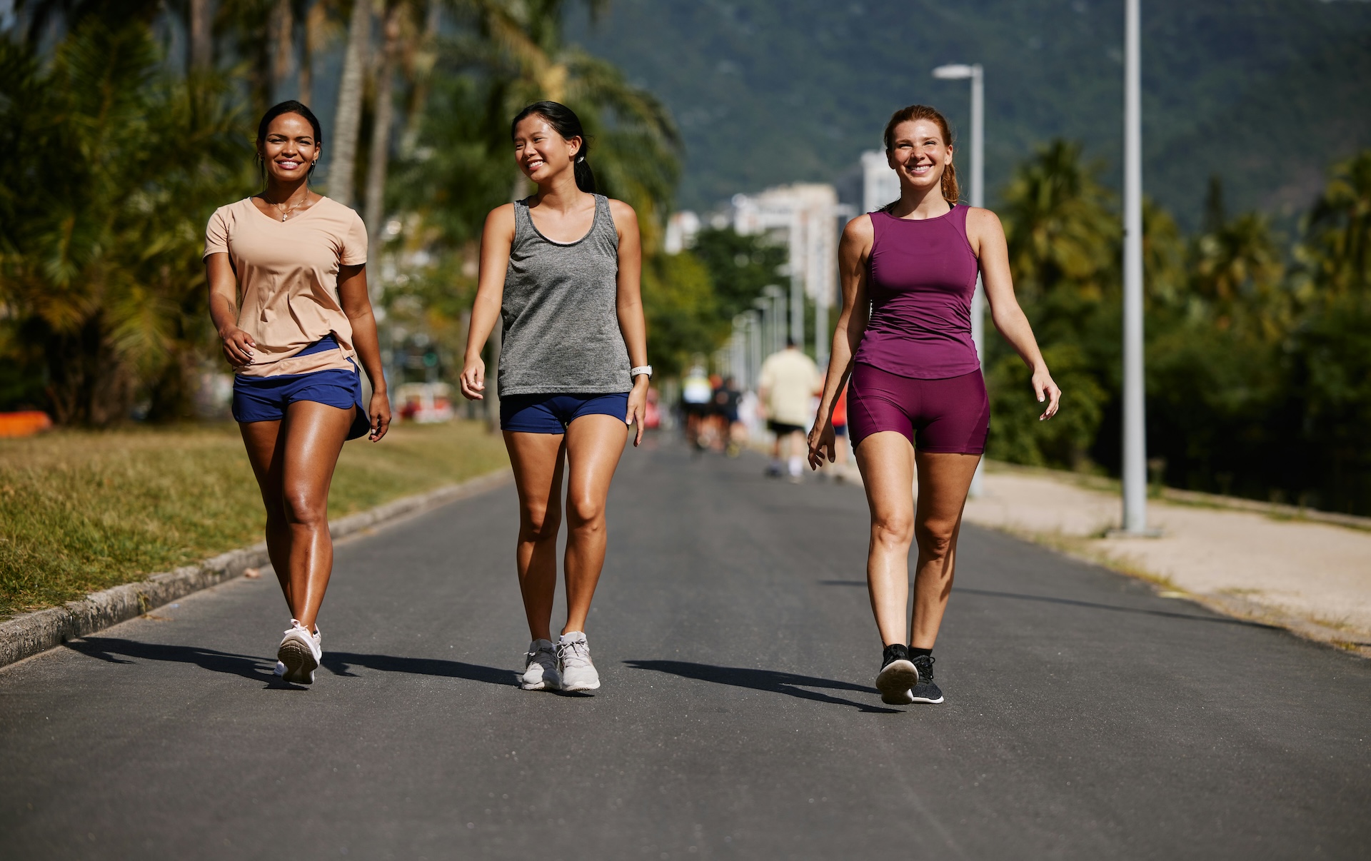 Three women walking briskly outdoors on a tree-lined path, exploring whether does walking build muscle when paired with pace and terrain changes