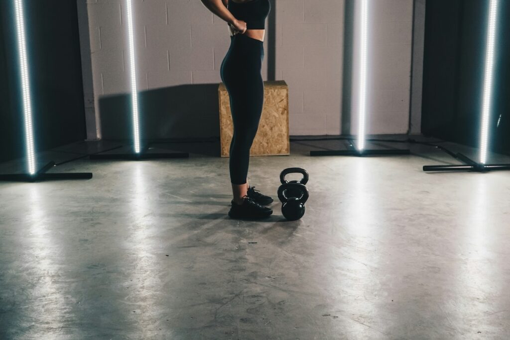 Woman in leggings standing next to kettlebells in gym, illustrating how long does it take to grow glutes with strength training