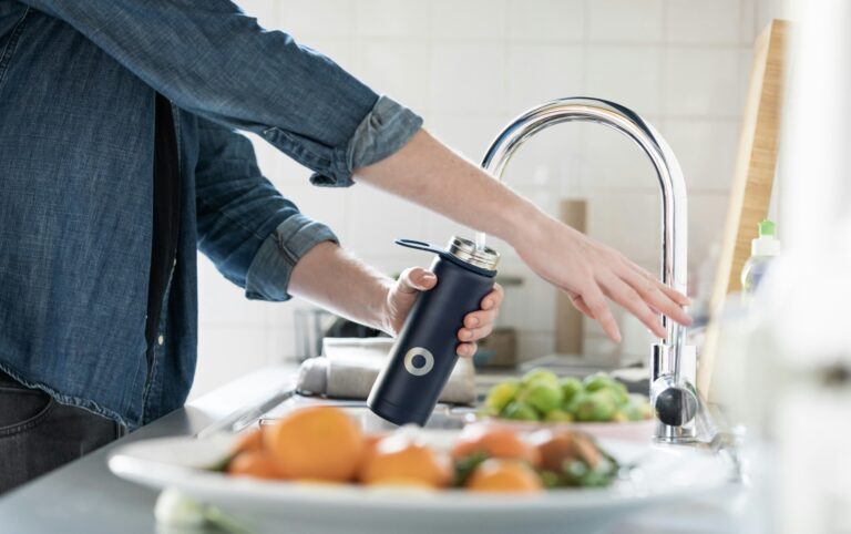 Person filling a reusable water bottle at the kitchen sink, a simple daily habit that supports efforts to reduce PFAS exposure