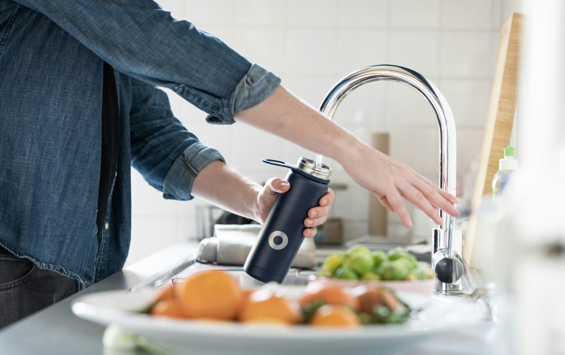 Person filling a reusable water bottle at the kitchen sink, a simple daily habit that supports efforts to reduce PFAS exposure