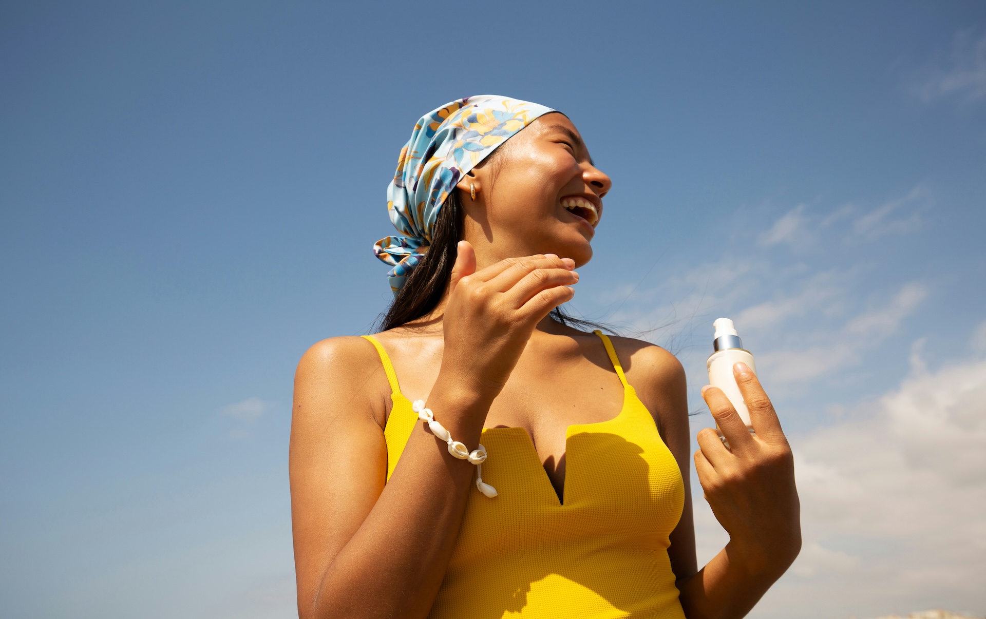 Woman applying safe sunscreen to her face while smiling outdoors in sunlight