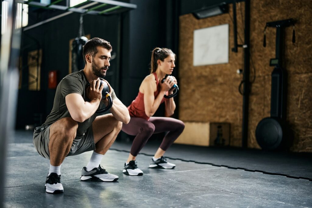 Man and woman performing goblet squats with kettlebells at the gym, building lower-body strength as part of learning how to build upper glutes
