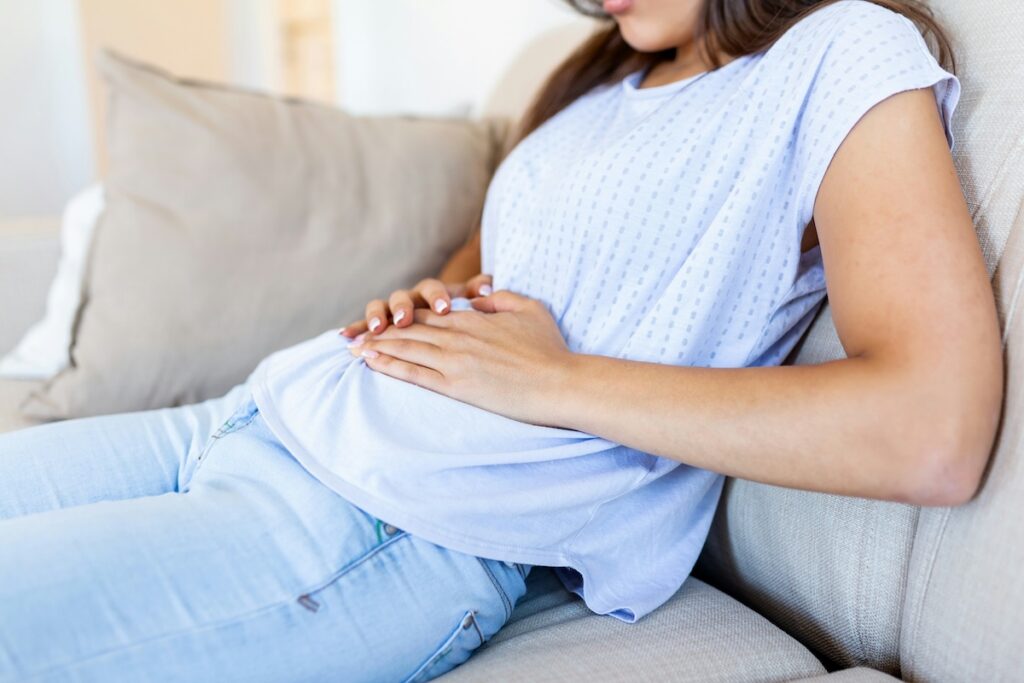 a woman grabs her stomach as she worries about how cortisol may impact her abdominal fat