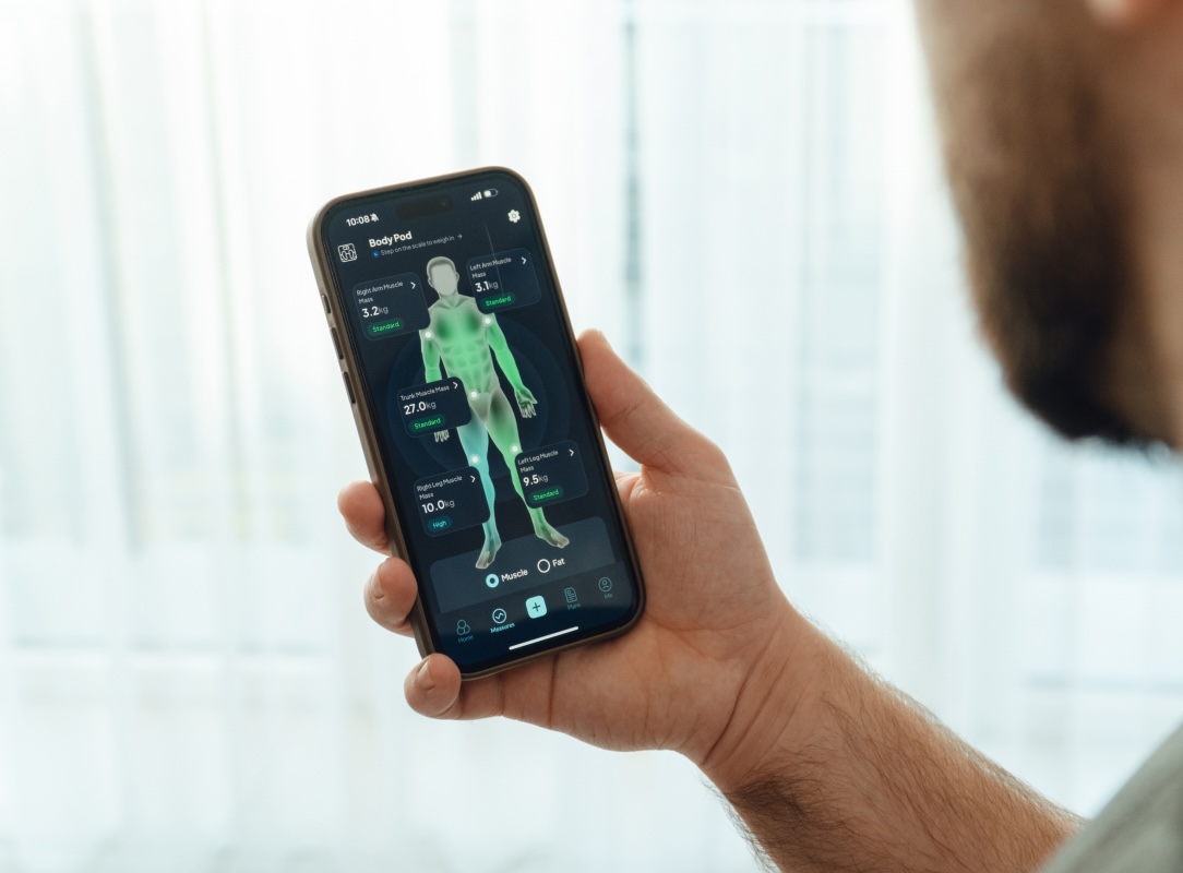 A person holding a phone displaying a health app with a digital outline of a human body and body composition metrics.