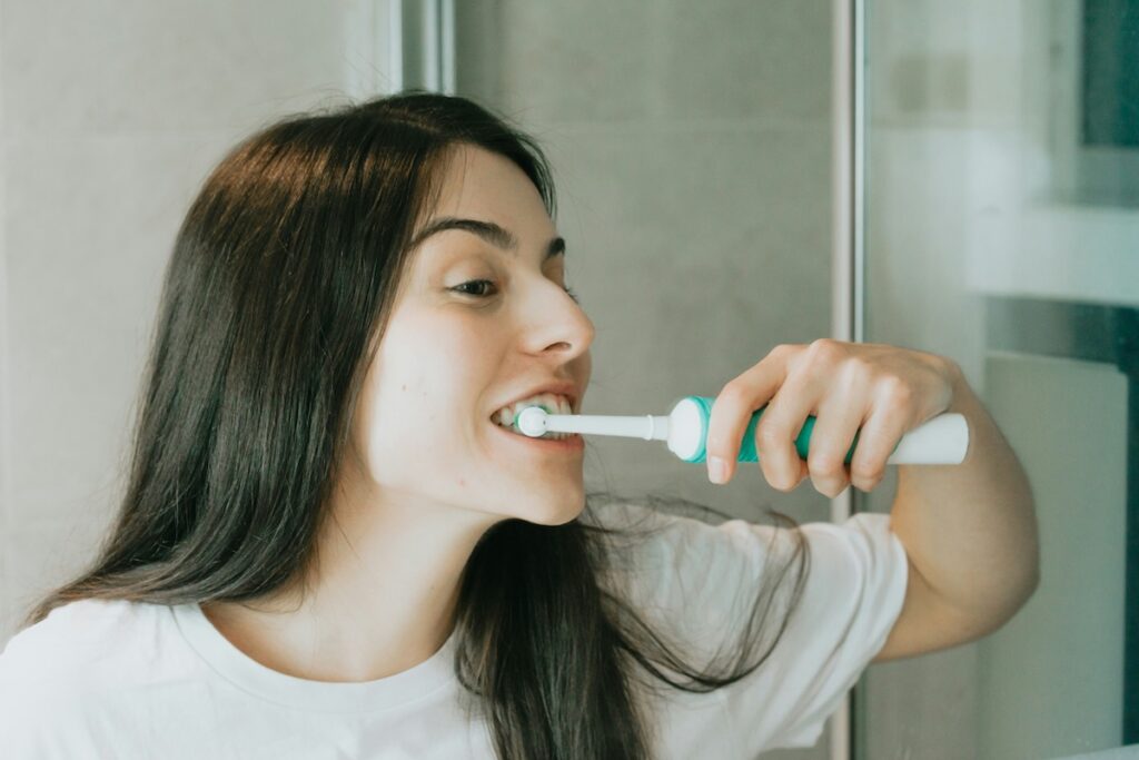 Woman brushing with electric toothbrush, one of the habits that damage teeth