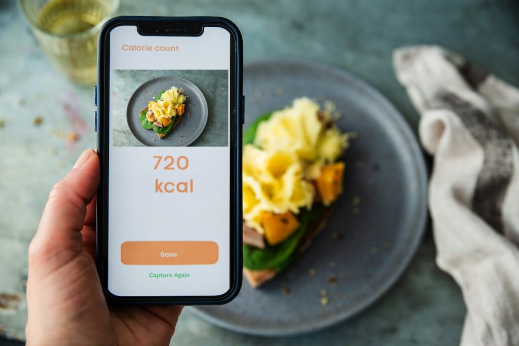Person tracking calories on phone app while eating a meal, reflecting the mindful approach that shaped why I stopped intermittent fasting