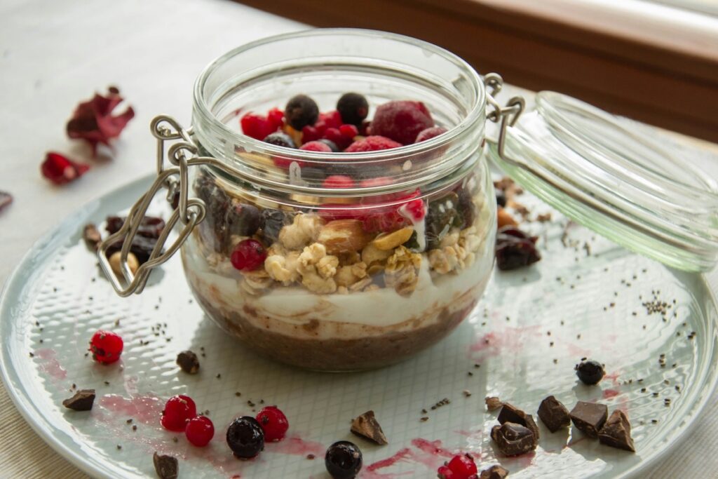 Layered high-protein overnight oats in a glass jar topped with granola, mixed berries, and chocolate shavings