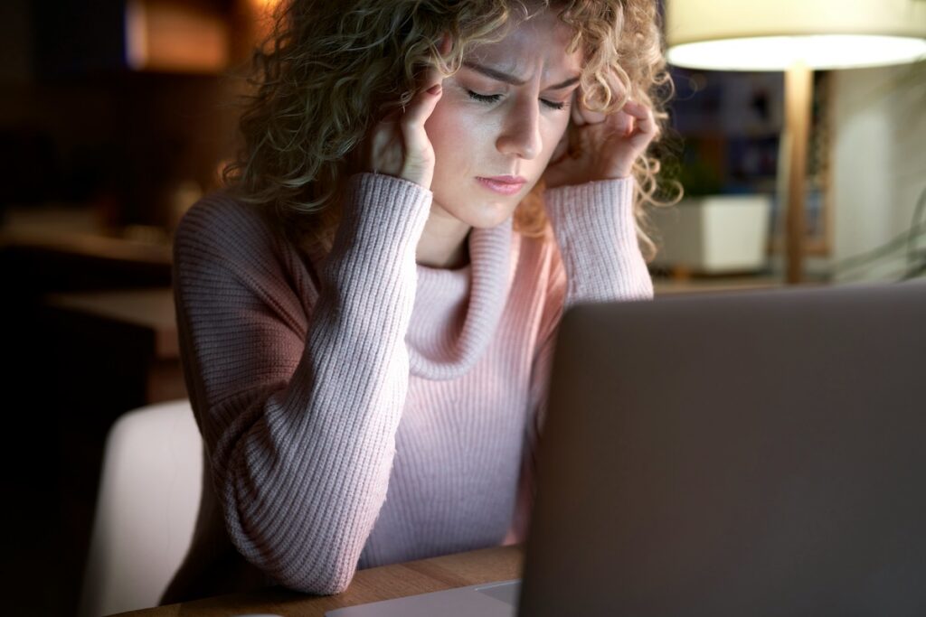 Stressed woman working late at a laptop, chronic stress that can raise cortisol and contribute to hormonal belly