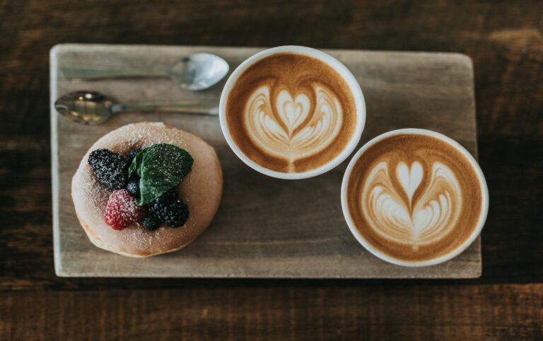 Two latte art coffees next to a berry-topped pancake, illustrating the coffee before or after breakfast question