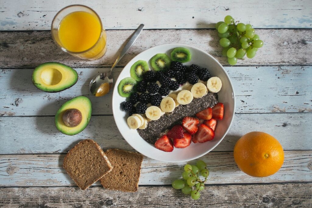 Fiber-rich spread for high protein vegetarian meals, including a fruit and chia bowl, avocado, whole-grain bread, and orange juice