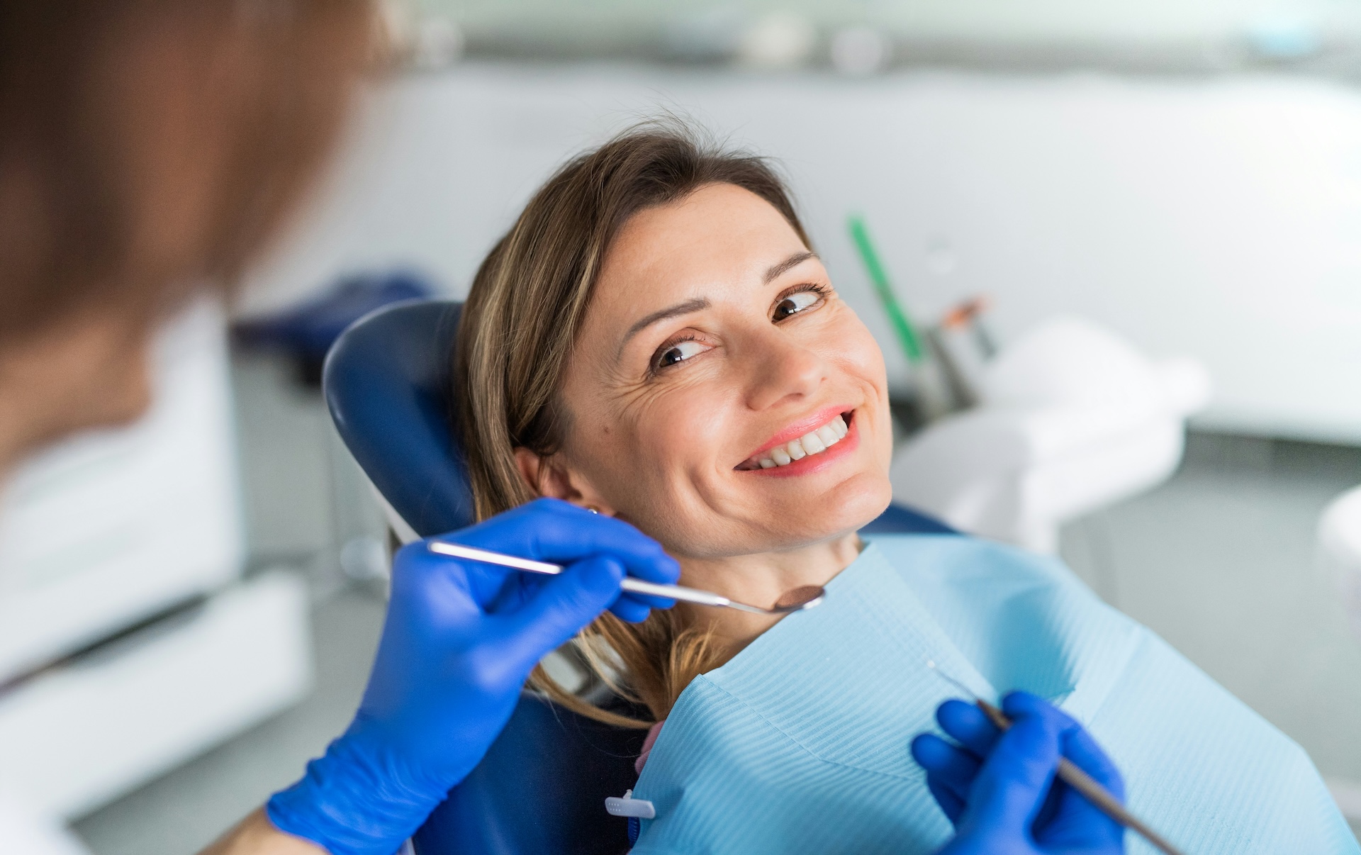 Woman smiling at dentist during checkup, discussing habits that damage teeth