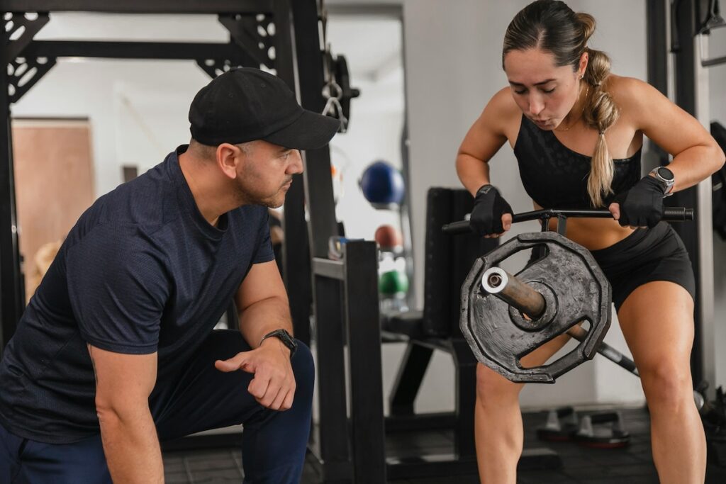 Trainer coaching a woman through a heavy barbell row, the kind of exercise and gut health researchers linked to higher beneficial gut bacteria