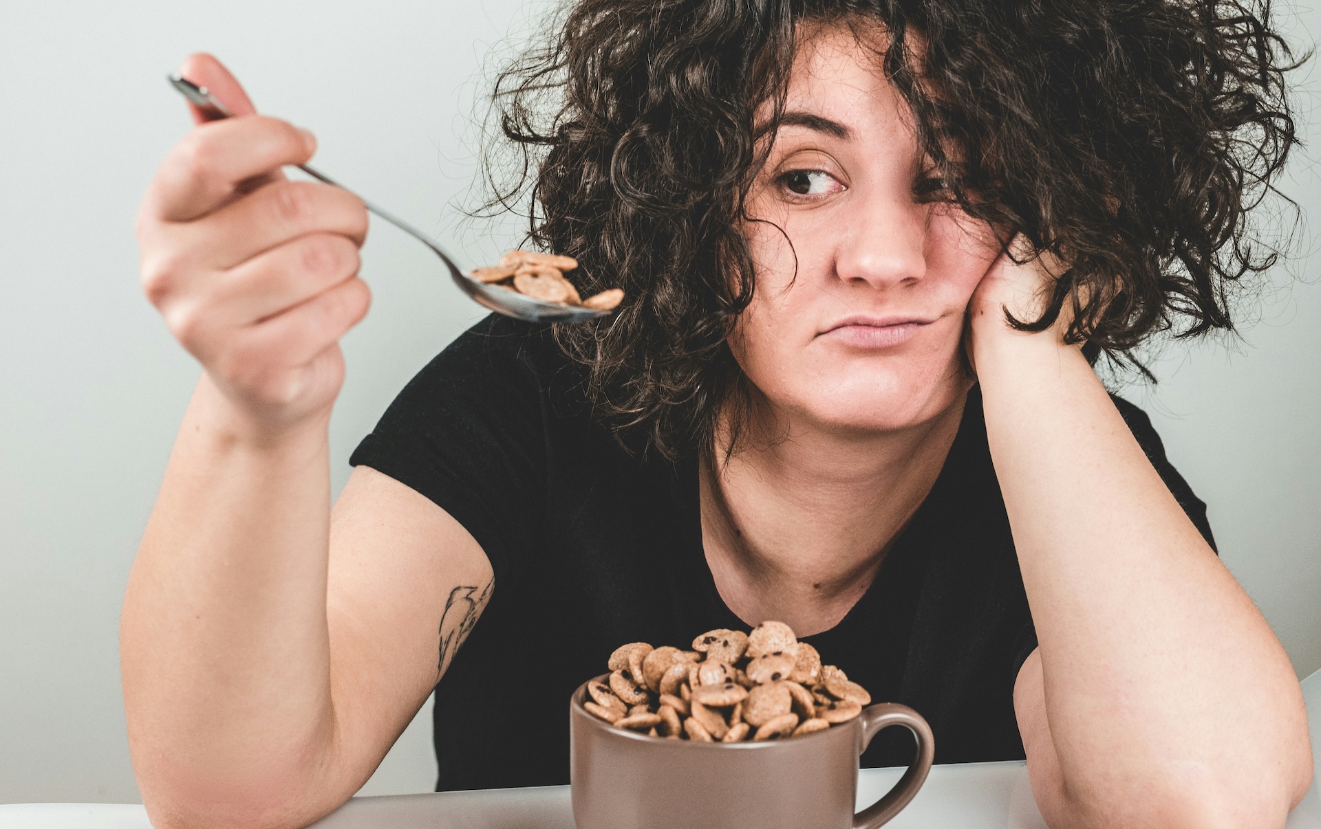 Woman eating cereal reluctantly with tired expression, reflecting irregular eating and depression risk from skipped meals