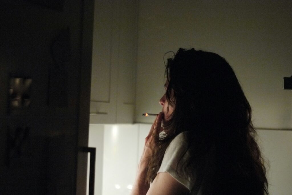 Woman standing in dark kitchen at night smoking, illustrating irregular eating and depression risk linked to late-night habits