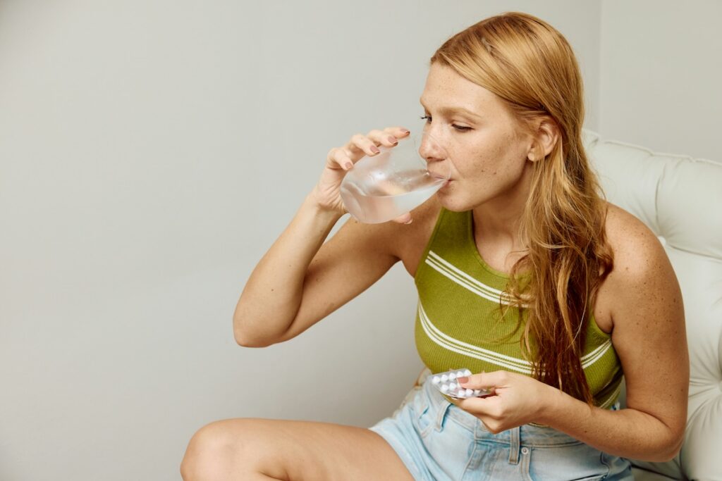 Woman drinking water and holding supplements while managing symptoms of low electrolytes