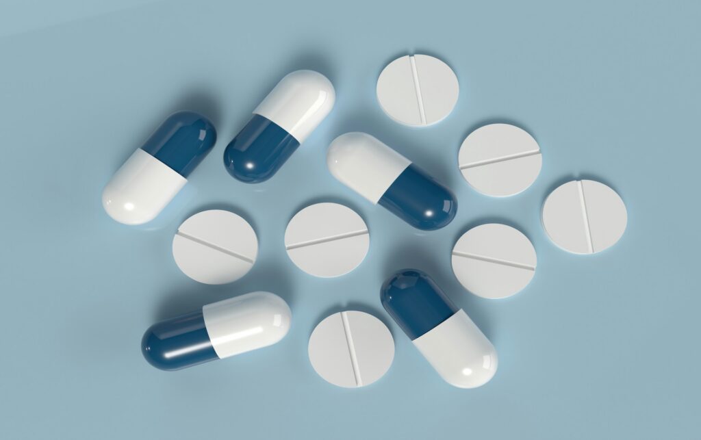 Blue-and-white metformin capsules and white scored tablets scattered on a light blue background, representing the diabetes drug inspired by goat's rue
