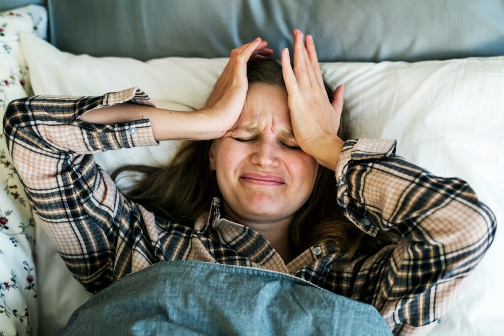 Woman lying in bed with hands on head showing signs of sleep deprivation and frustration