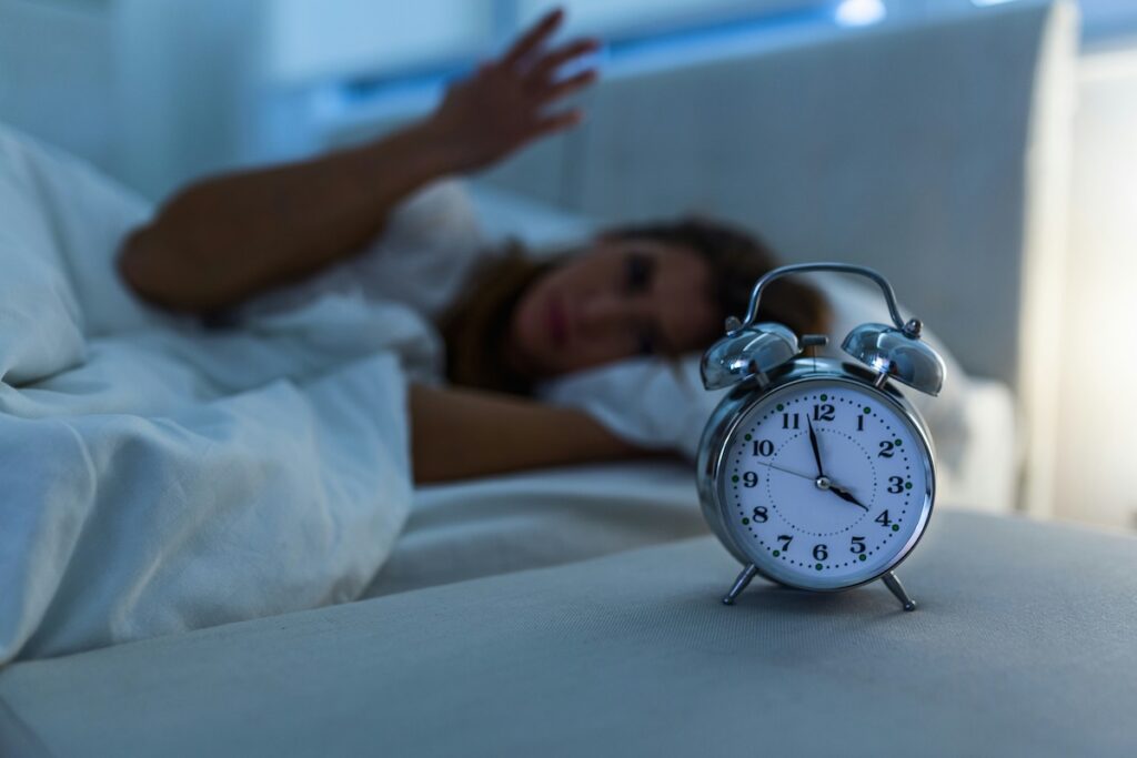 Woman reaching for alarm clock after too little sleep, one of the habits that raise blood pressure