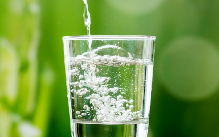 Clear glass filling with clean water, representing the goal of choosing water filters for microplastics to keep drinking water safe