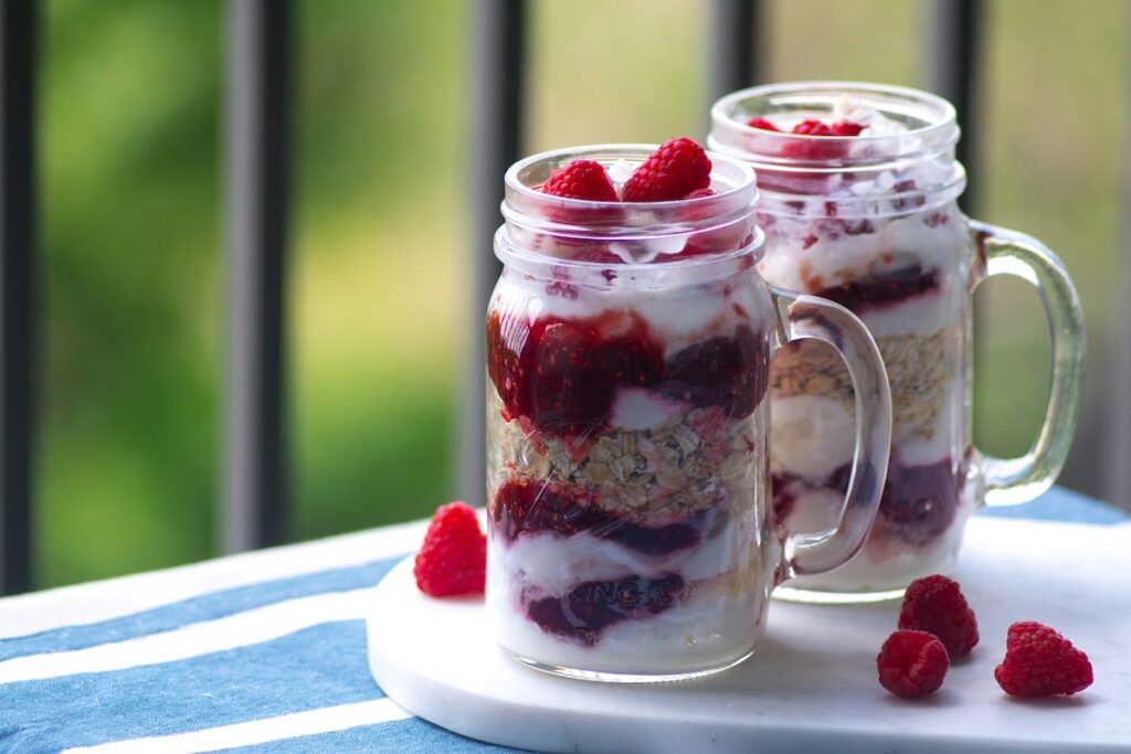 Mason jars layered with berry overnight oats and raspberries, a low calorie meals option for breakfast
