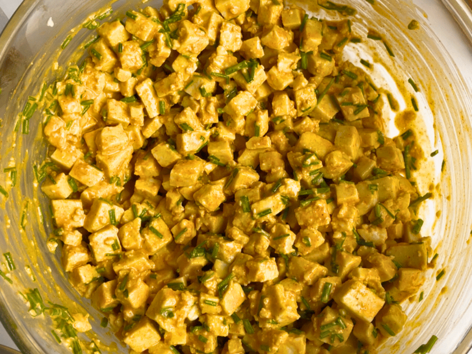 Vegan egg salad in a glass mixing bowl with cubed tofu, fresh chives, and turmeric for a golden, eggy look