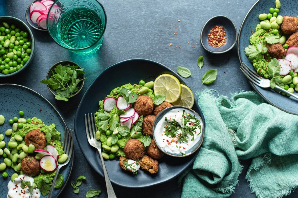 High-protein foods including falafel, edamame, and Greek yogurt dip served over smashed peas with radish and lime