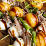 Close-up of melon caprese skewers with cantaloupe, mozzarella, prosciutto, and basil drizzled in balsamic glaze
