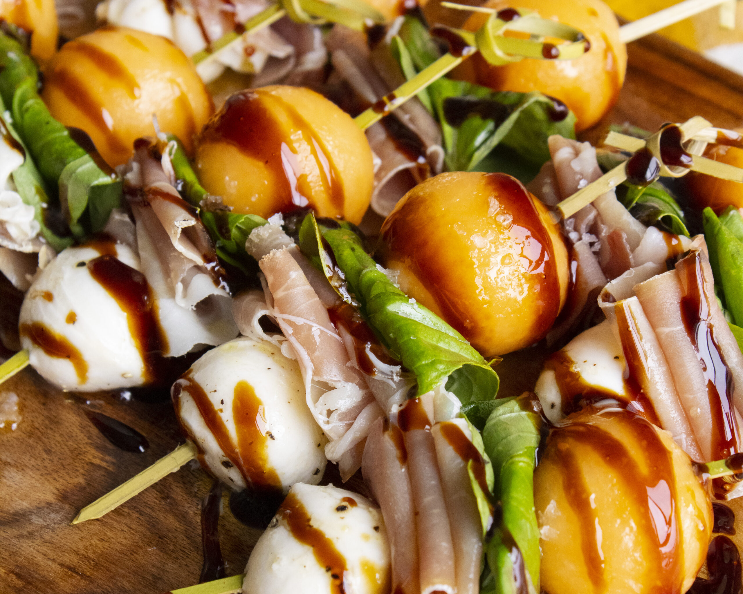 Close-up of melon caprese skewers with cantaloupe, mozzarella, prosciutto, and basil drizzled in balsamic glaze