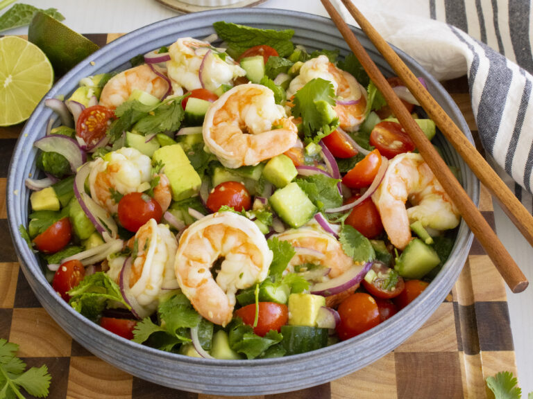 Vietnamese shrimp salad with poached shrimp, avocado, cucumber, cherry tomatoes, red onion, and fresh herbs in a blue bowl with chopsticks and lime