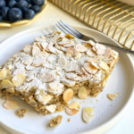 Almond croissant baked oats topped with toasted almond slices and powdered sugar, served on a white plate with fresh blueberries