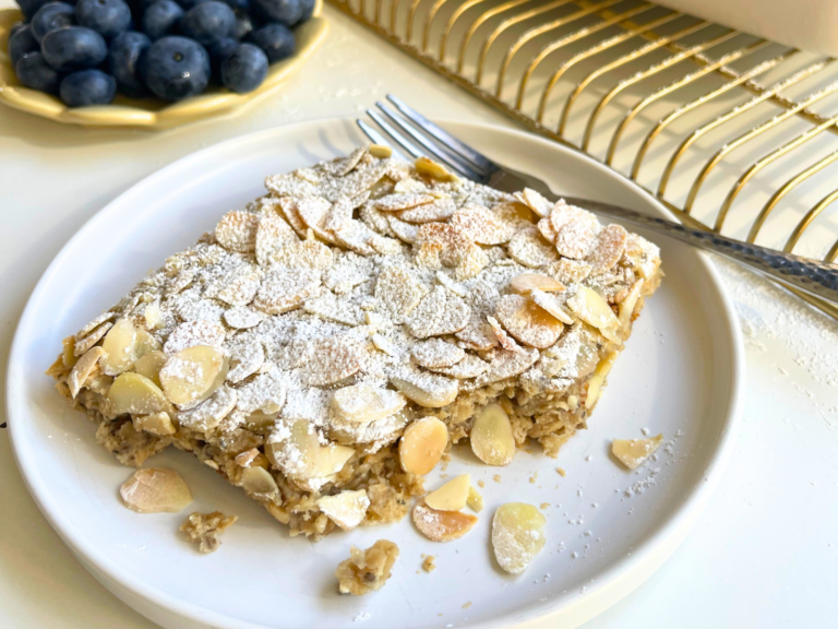 Almond croissant baked oats topped with toasted almond slices and powdered sugar, served on a white plate with fresh blueberries
