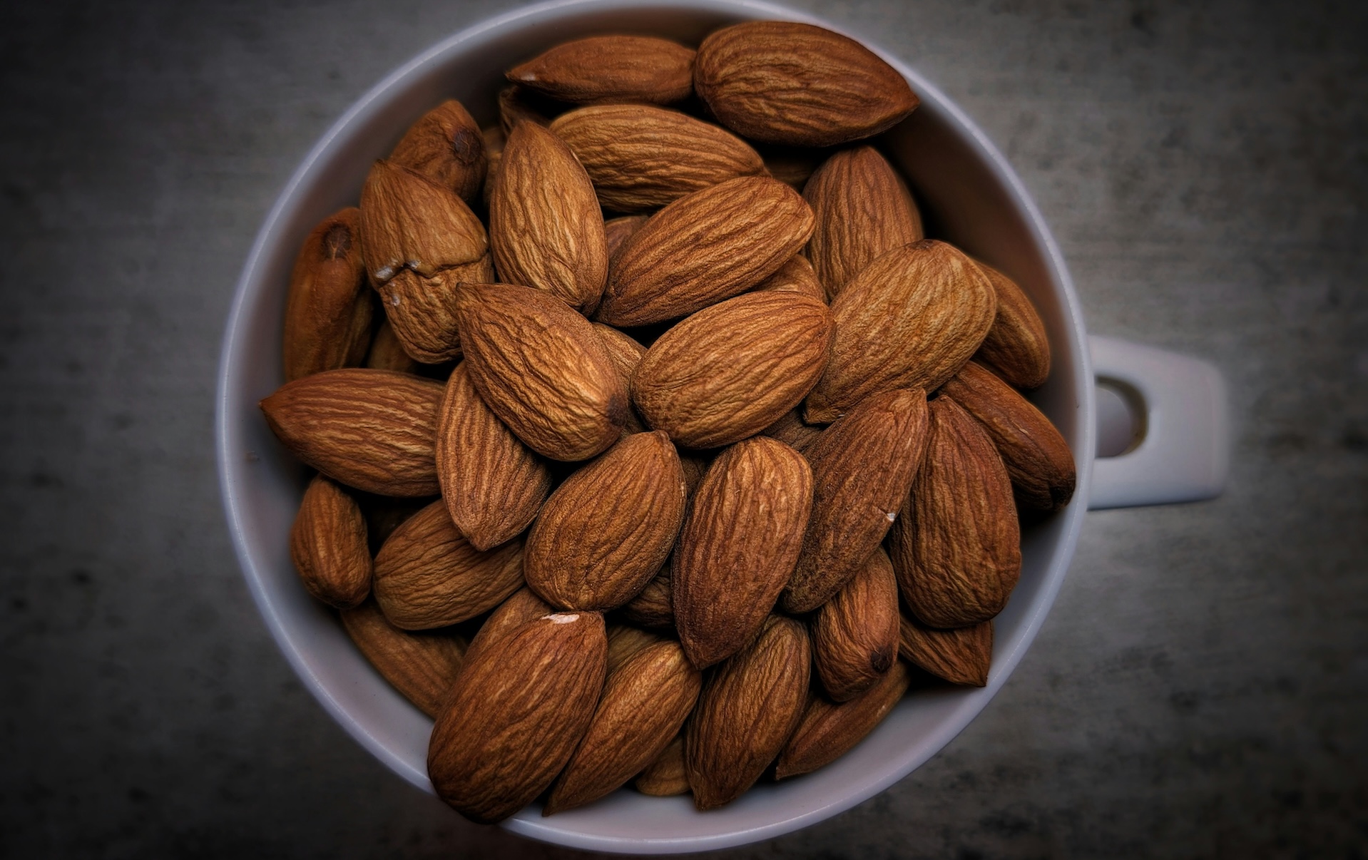 Overhead view of whole raw almonds filling a white mug, showcasing the healthiest nut you can eat