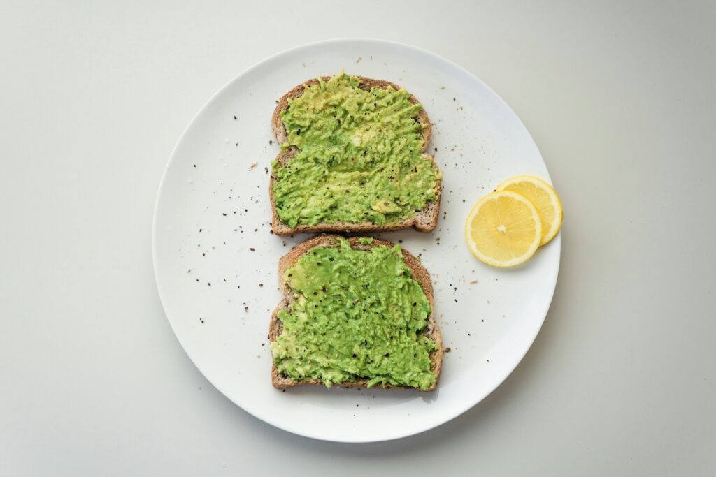 Two slices of avocado toast with lemon on a white plate.