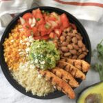 chipotle chicken burrito bowl with grilled chicken strips, brown rice, pinto beans, pico de gallo, guacamole, and charred corn in a black bowl