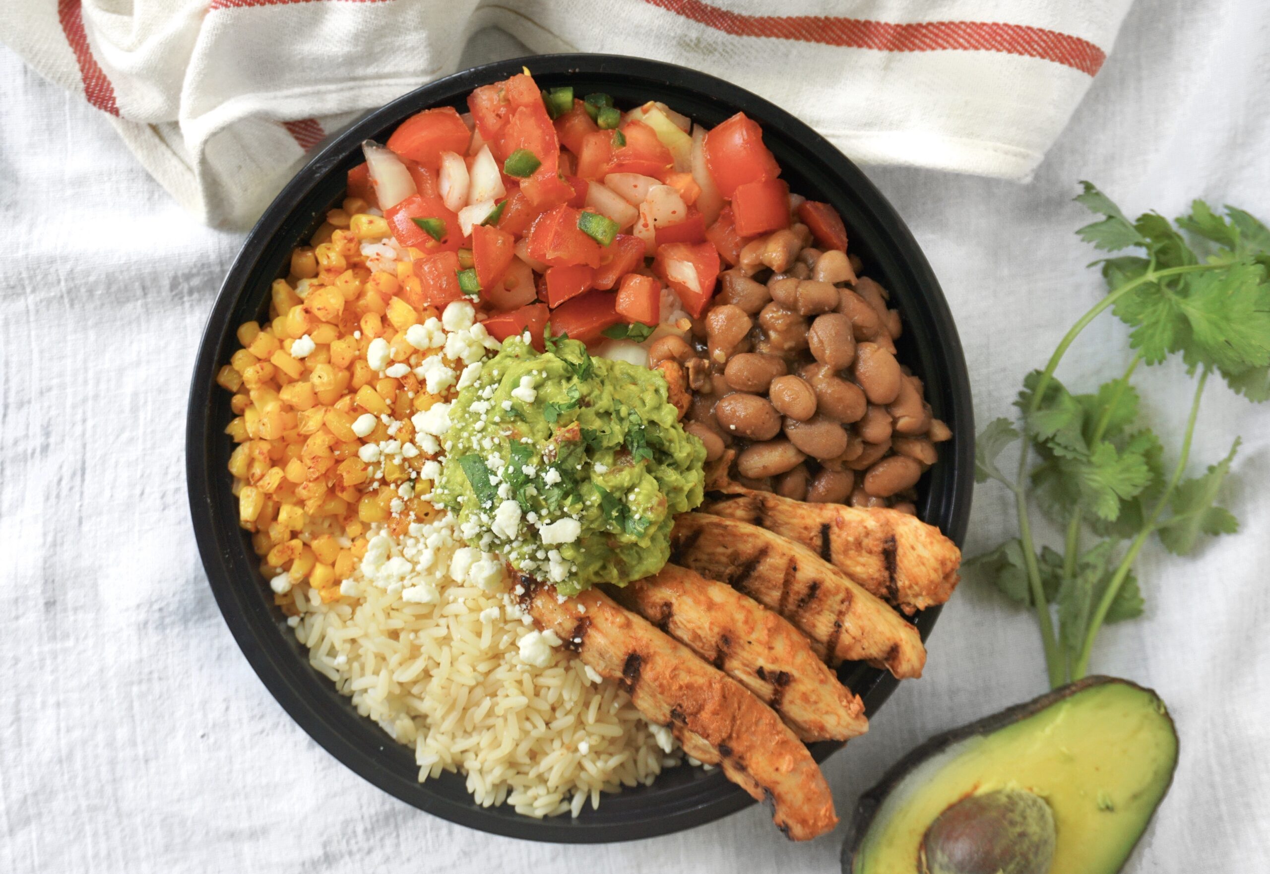 chipotle chicken burrito bowl with grilled chicken strips, brown rice, pinto beans, pico de gallo, guacamole, and charred corn in a black bowl