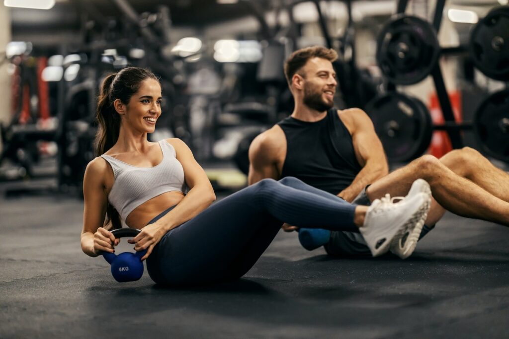 Two people performing kettlebell twists on a gym floor during a workout.