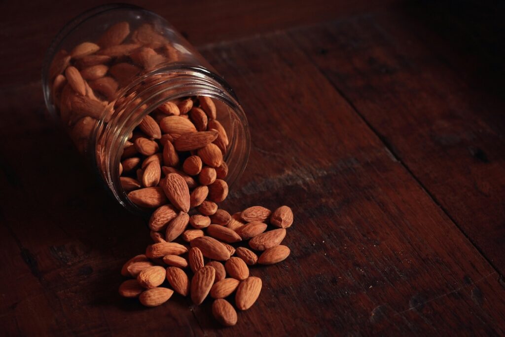 Jar of almonds spilled onto a wood table, the kind of drop that puts the five second rule to the test