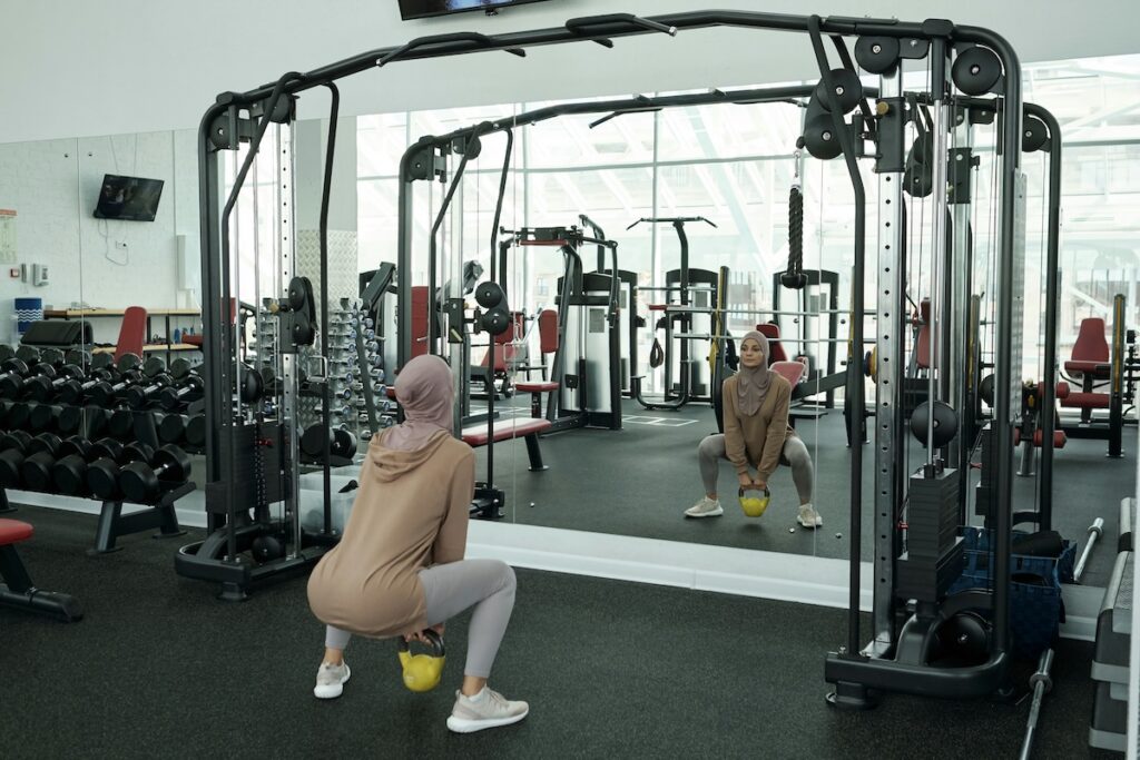 Woman in a headwrap performing a kettlebell squat in a gym in front of a mirror.
