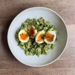Overhead view of Green Goddess Salad with jammy soft-boiled eggs, chives, and cracked black pepper in a white bowl.