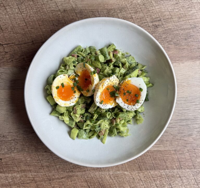 Overhead view of Green Goddess Salad with jammy soft-boiled eggs, chives, and cracked black pepper in a white bowl.