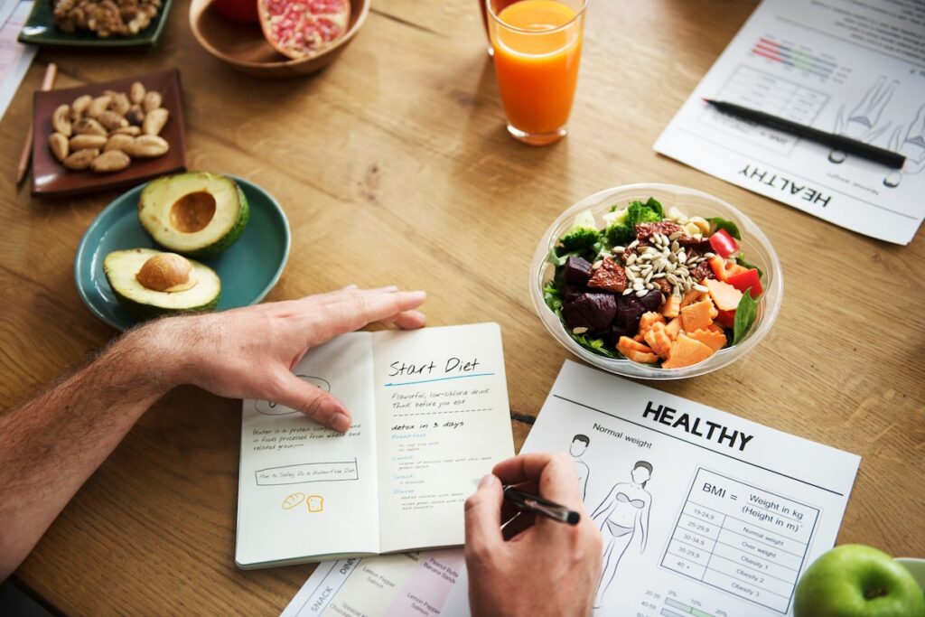 Person tracking meals in a journal alongside a fresh veggie bowl, part of a routine for how to fix your gut health