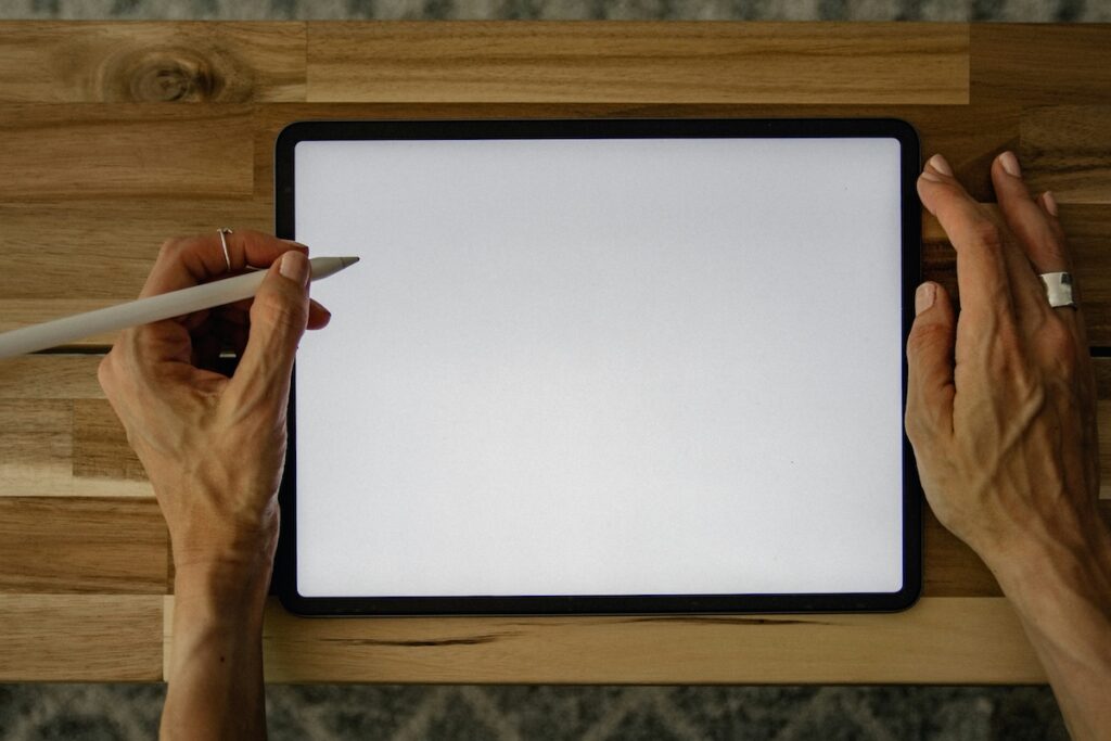 Older adult's hands using a stylus on a digital tablet, similar to tools used in handwriting and cognitive decline research.