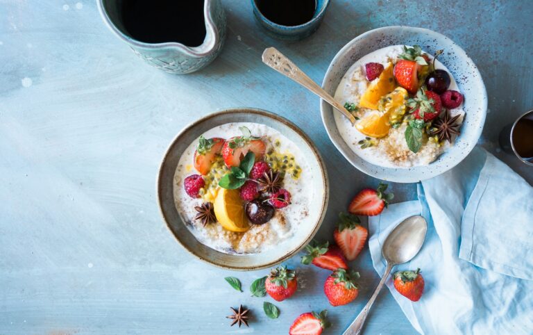 Two bowls of oatmeal topped with berries and sliced citrus on a blue tabletop.